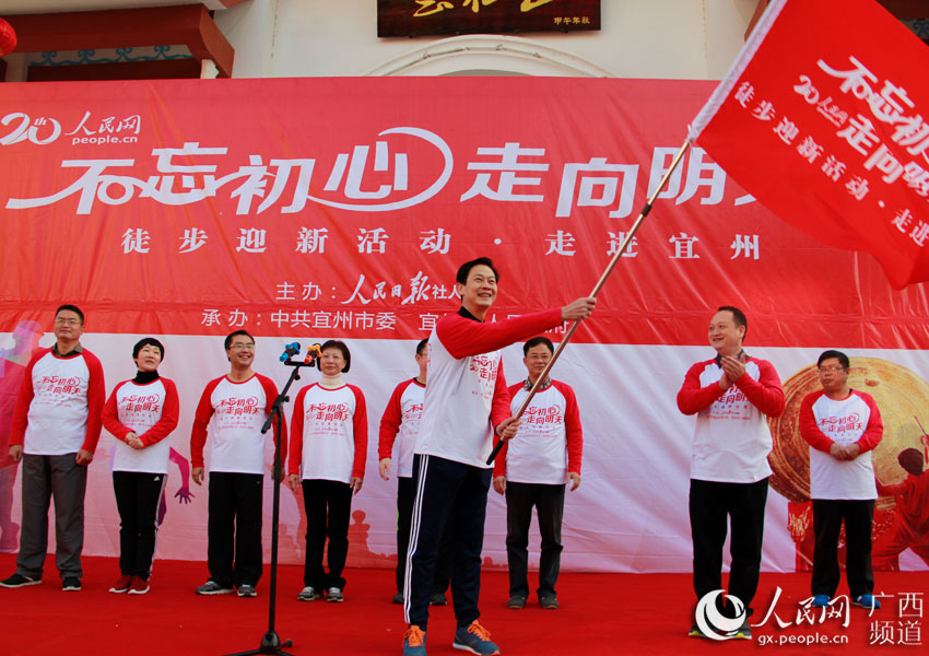 宜州市宣傳部部長、副市長蒙潤武從人民網代表手中接過“不忘初心-走向明天”徒步迎新活動旗幟。