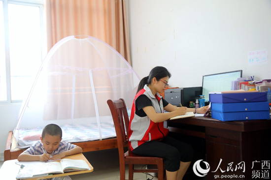 彭燕在休息室整理扶貧材料，兒子乖巧地在一旁寫作業。何正君攝