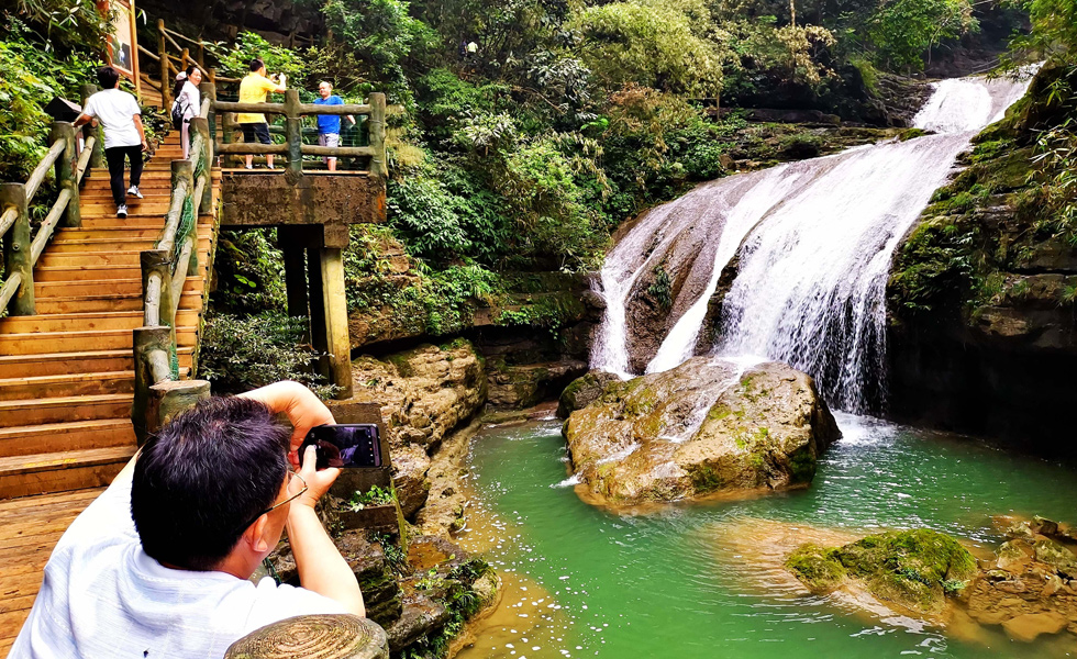 游客在環江毛南族自治縣牛角寨景區的“三疊泉”瀑布游玩拍照