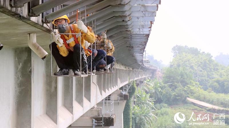 職工蹲在“吊籃”裡進行橋梁病害整修作業。譚育俊攝