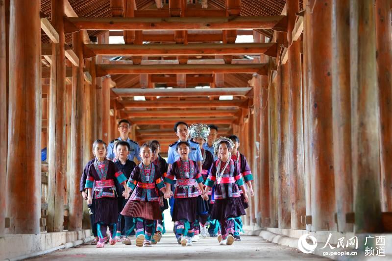 惠州邊檢站扶貧民警與侗族學童在風雨橋上手牽手唱童謠。 廖鍵攝