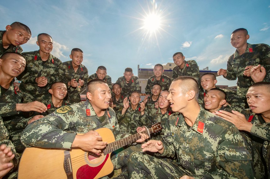 训练间隙，一名班长正在与新兵正在进行吉他弹唱。