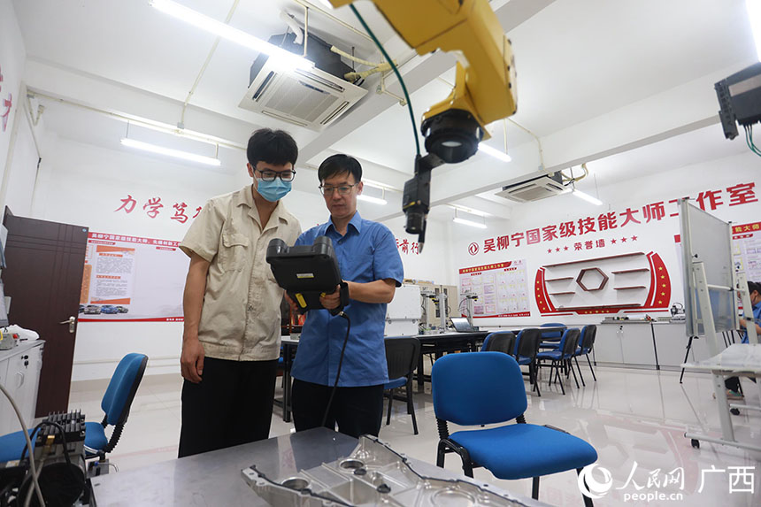 集中培訓后，發動機事業部的維修鉗工梁振林向吳柳寧請教工業機器人操作技術。