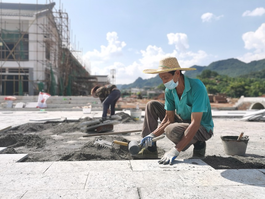 在宁明县乡村振兴创业街项目建设工地，工人们正顶着烈日进行广场地板铺设作业