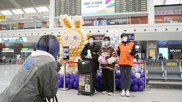 旅客与车站志愿者在兔年气球造型前合影。李俊鸣摄