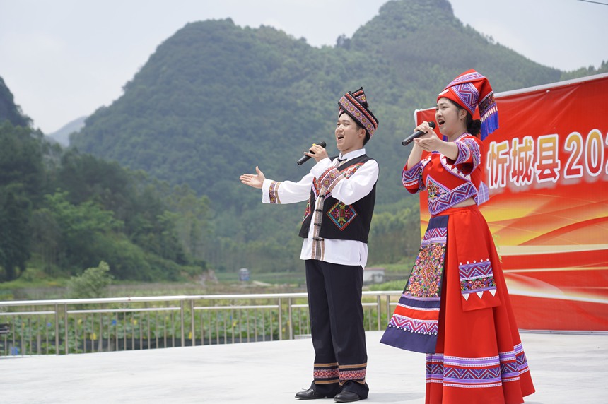 5月17日，在忻城縣大塘鎮六安村開展社會科學普及活動周暨全民藝術普及月基層文藝演出活動，圖為社科普及志願者為群眾演唱本土原創歌曲《我在忻城等你來》