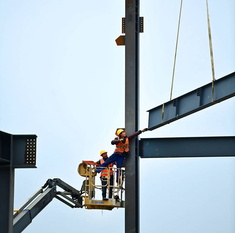 项目建设正酣，工人吊装钢架构忙碌。黄蕊摄