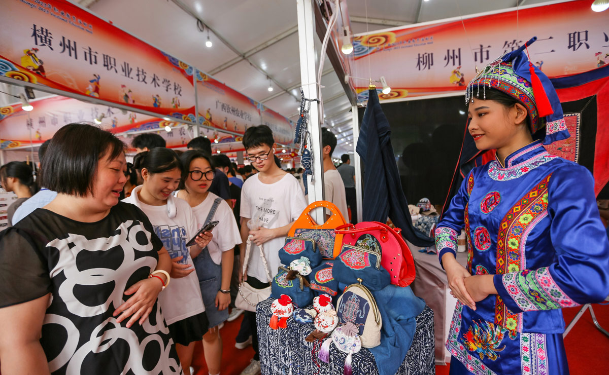 柳州市第二职业技术学校学生在展示手工制作的民族小提包