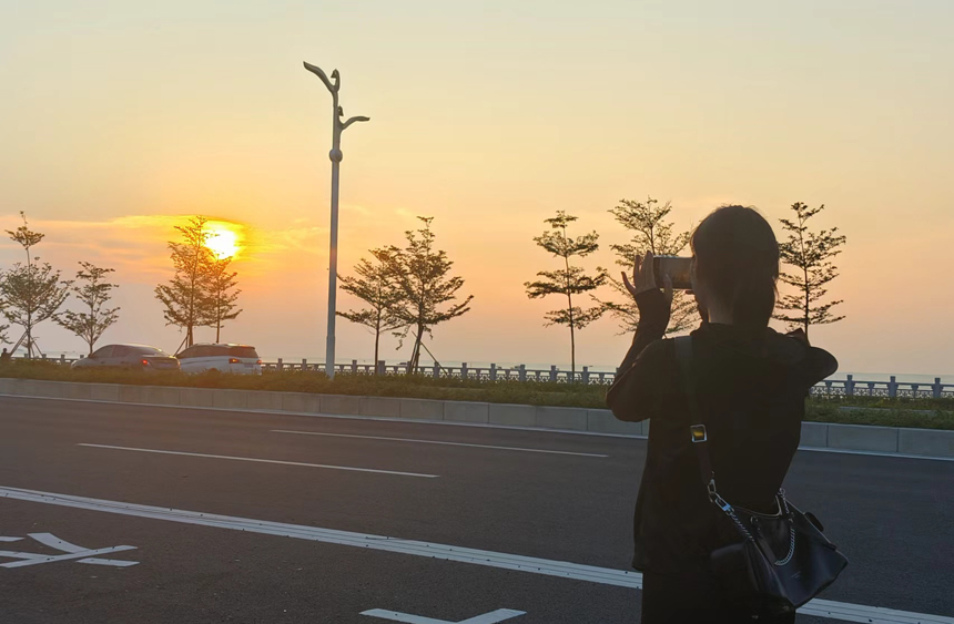 游客在廉州湾大道上拍落日