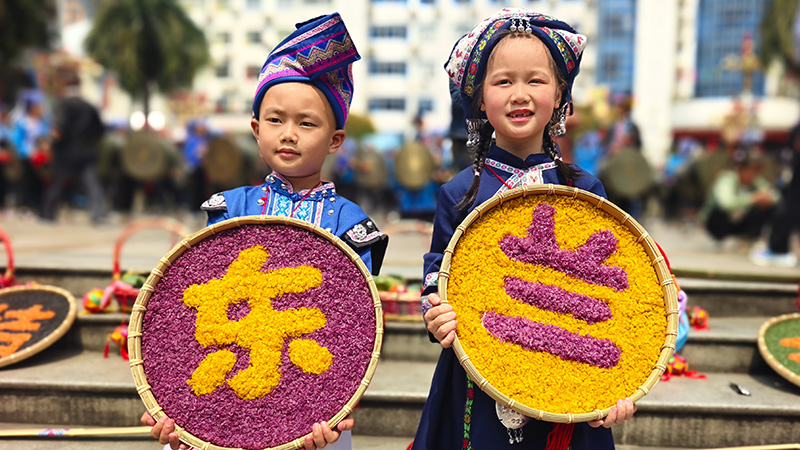 3月26日，广西东兰县的两名小朋友在展示写有”东兰“字样的五色糯米饭。高东风摄