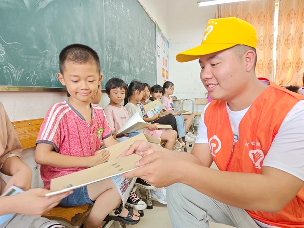 图为青年志愿者向学生发放爱路护路知识笔记本。徐柯摄