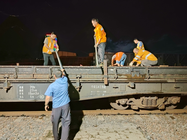 该段职工正在传递防洪料具装上轨道作业车。