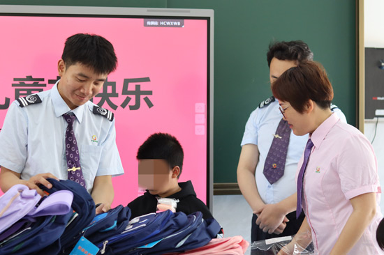 图为：工作人员给孩子们送书包（图片署名：唐运荷）