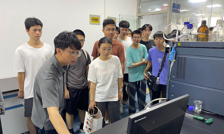 来宾监测中心技术人员（左一）向参观学习的大学生介绍大型仪器的使用要点