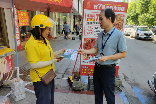 图为执法人员（右一）向社区居民发放电子烟危害宣传单-王强秀 摄