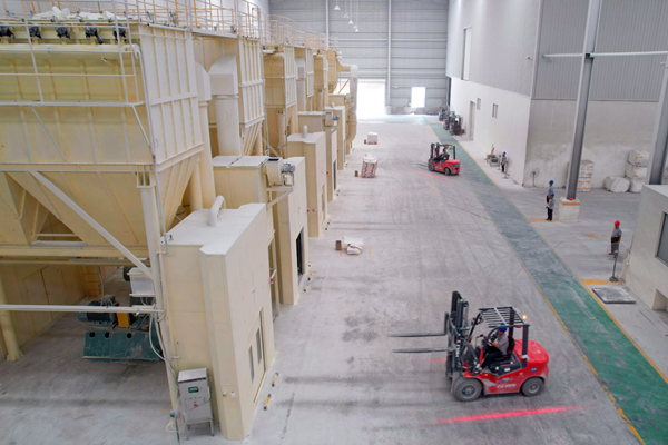 廣西隆升新材料有限公司生產車間內，工人使用機械臂搬運碳酸鈣粉體產品。
