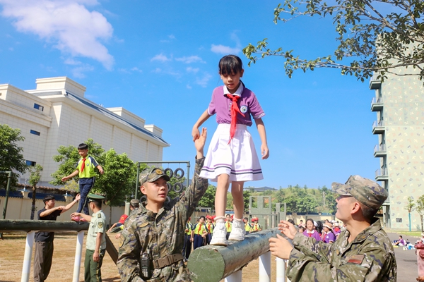 武警官兵攙扶小朋友過四百米障礙的獨木橋。