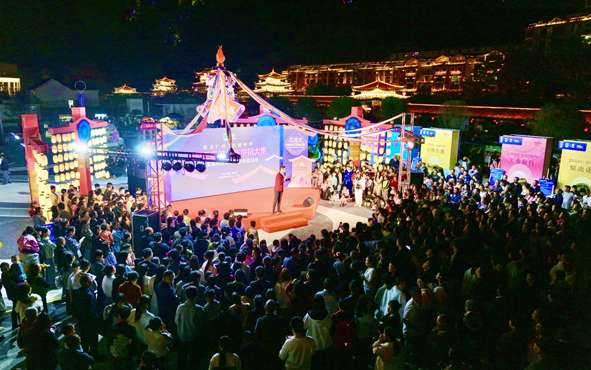 随着夜幕降临，灯光渐次亮起，一场融合民俗表演与趣味拍卖的夜间盛宴正在举办。