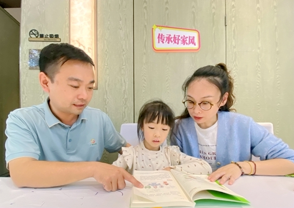 图为李翔夫妻引导女儿阅读书籍。
