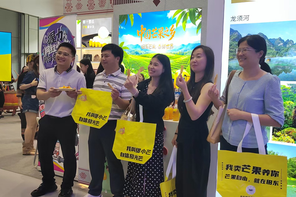 游客品尝芒果冻干并合影。周月珍摄