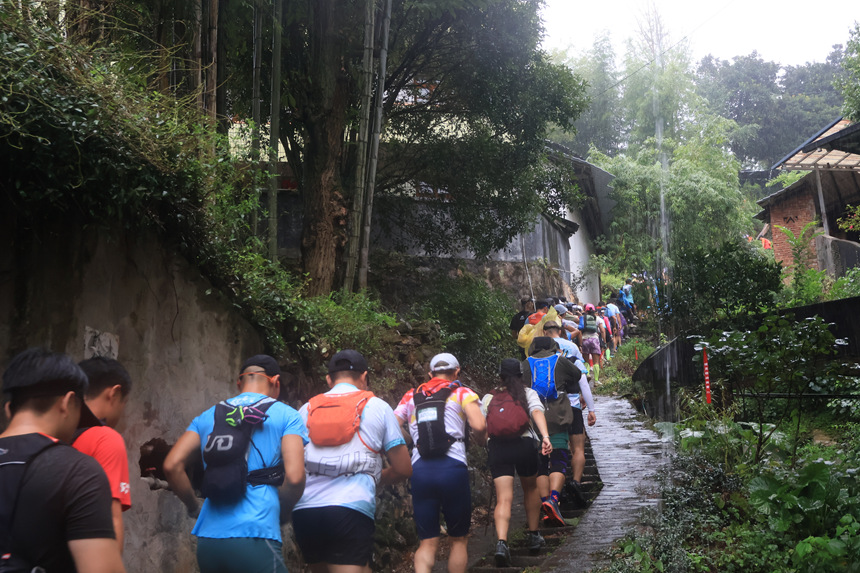选手们正在通过民居旁的小路，准备登山。