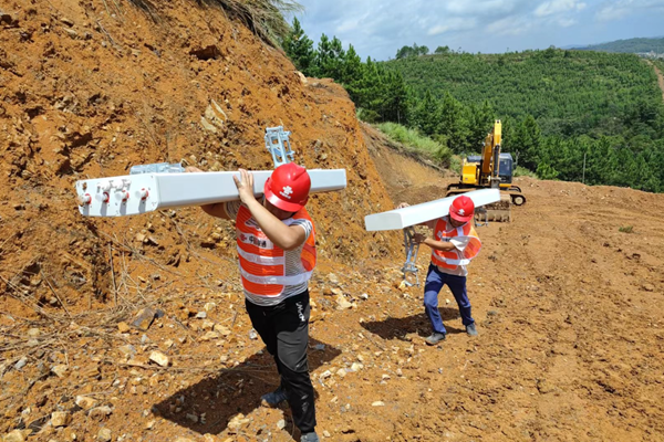 中国联通网络建设人员肩扛网络设备，吃力地走在泥泞不平的上山路，进一步加快世纪工程建设。中国联通供图