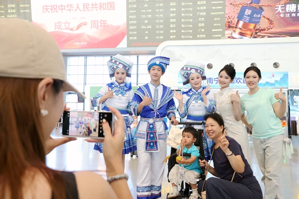 旅客与身着民族服饰的表演人员合影留念。谭媛元摄